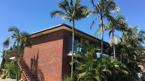 A two-story brick building with a flat roof, a staircase on the left, and palm trees surrounding the property. - Centenary Motor Inn (Oxley)