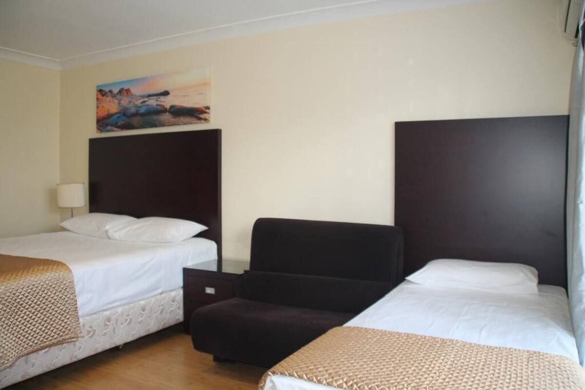 A hotel room with two single beds, a dark headboard, a small armchair, and a painting on the wall.