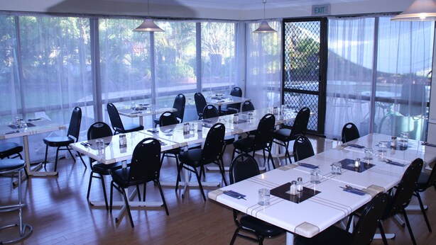 A conference room with multiple tables and chairs, large windows with curtains, and an exit sign. - Centenary Motor Inn (Oxley)