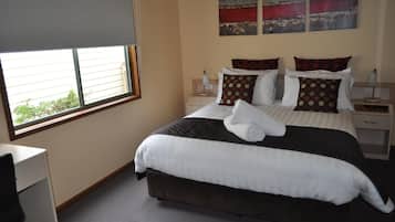 A neatly made bed with white and brown bedding, two bedside tables with lamps, and a window with blinds.