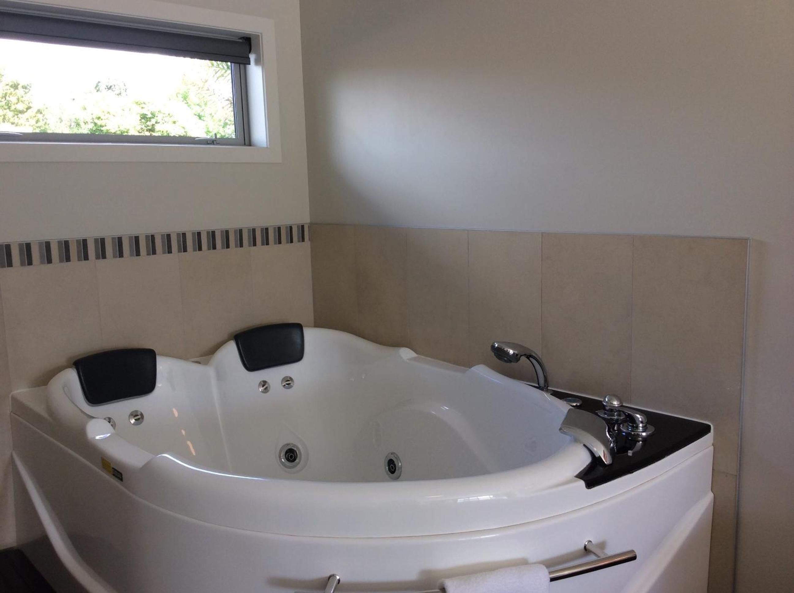 A white freestanding bathtub with a black seat, a showerhead, and a towel rack.