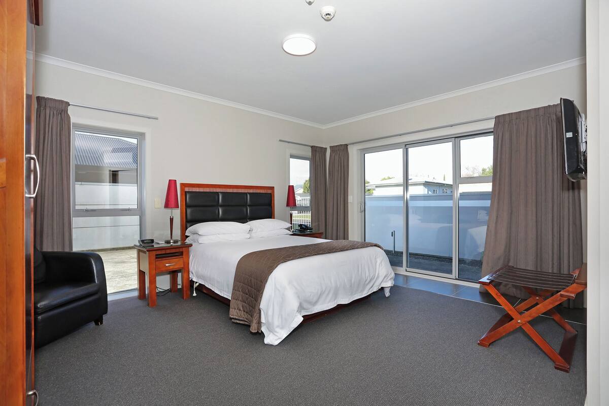 A hotel room with a large bed, a desk with a lamp, a chair, and a TV.