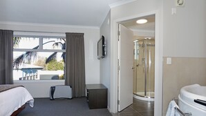 A hotel room with a bed, a desk, a TV, a shower, and a view of the outside. - City Corporate Motor Inn (Palmerston North)