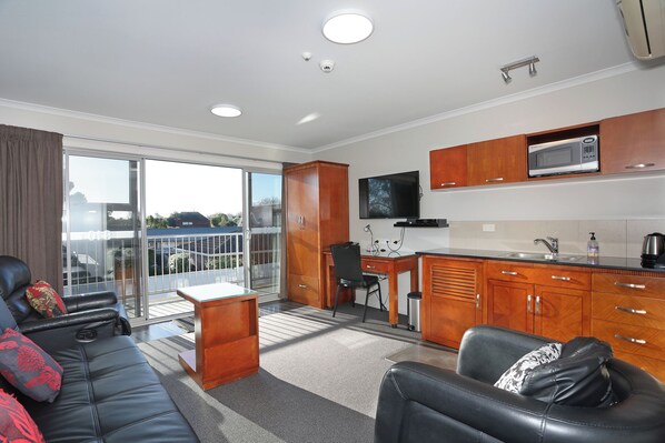A modern living room with a sofa and a coffee table, a kitchen with wooden cabinets and a microwave, and a balcony with a view. - City Corporate Motor Inn (Palmerston North)