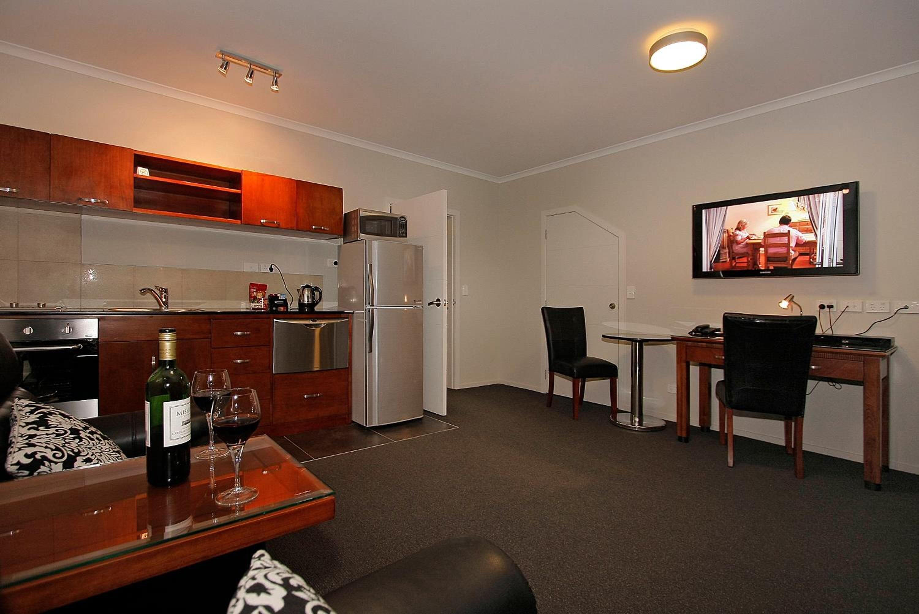Un espacio habitable compacto con kitchenette, comedor y televisor montado en la pared.