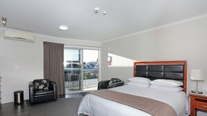 A hotel room with a large bed, a chair, a small table, and a view of the outside. - City Corporate Motor Inn (Palmerston North)