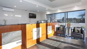 A reception area with a wooden reception desk, a flat-screen TV, a small table with a plant, and two leather armchairs. - City Corporate Motor Inn (Palmerston North)