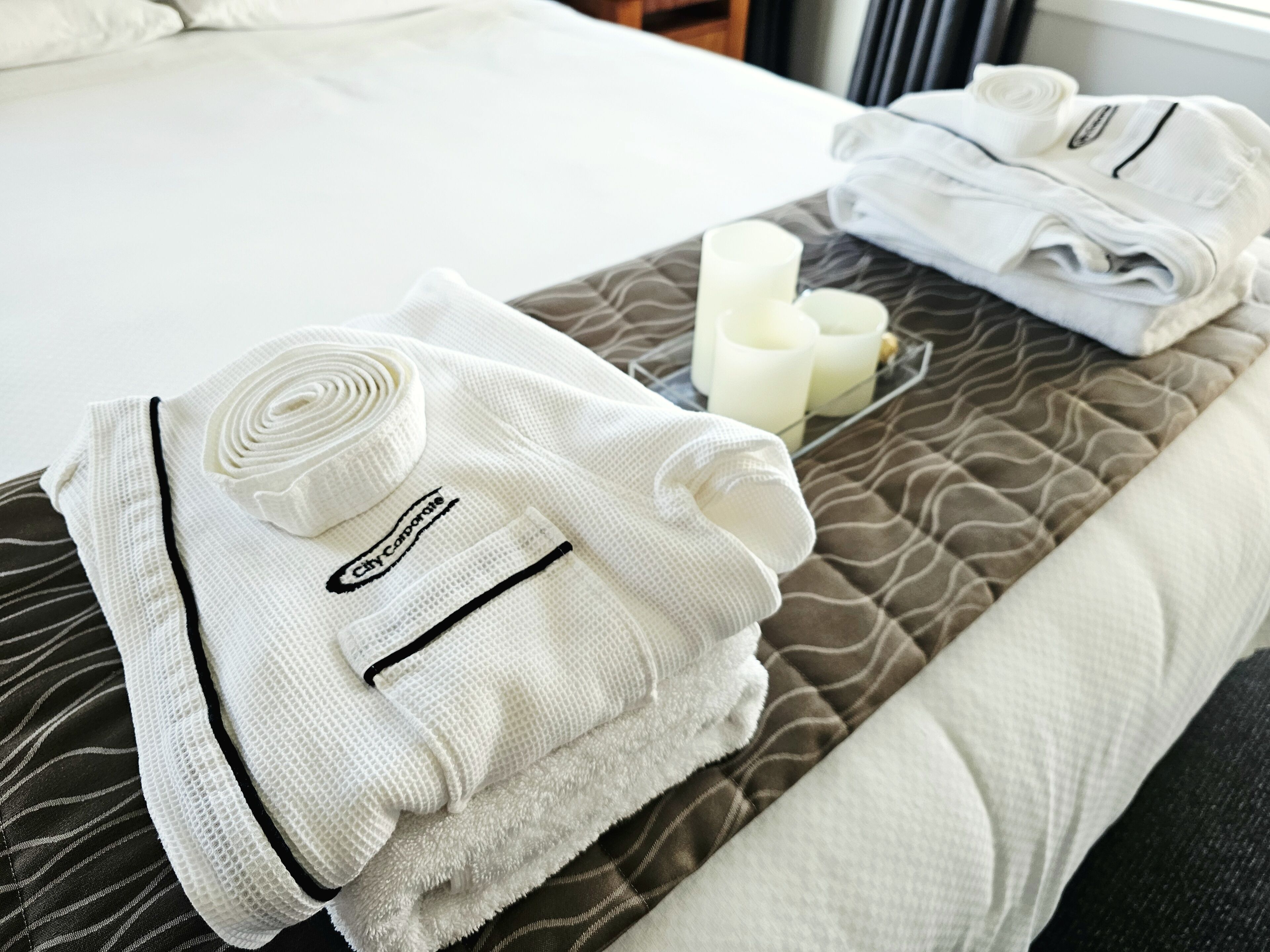 Toallas ordenadas y una vela sobre una cama con edredón estampado.