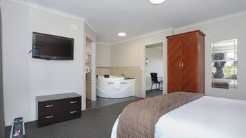 A hotel room with a bed, a TV, a desk with drawers, a chair, a large wooden wardrobe, and a bathroom with a bathtub and sink.