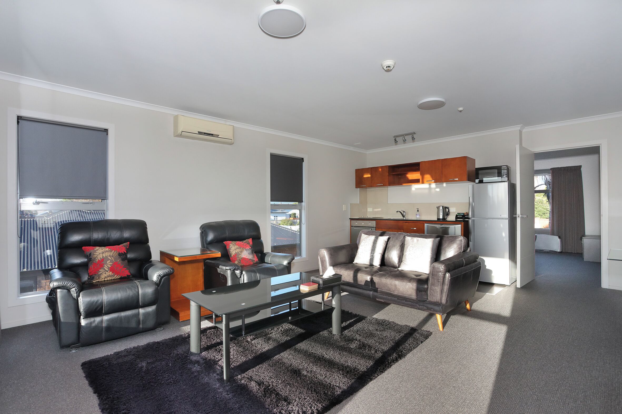 A modern living room with a sofa, armchair, and coffee table. There is a kitchen area with cabinets and appliances.