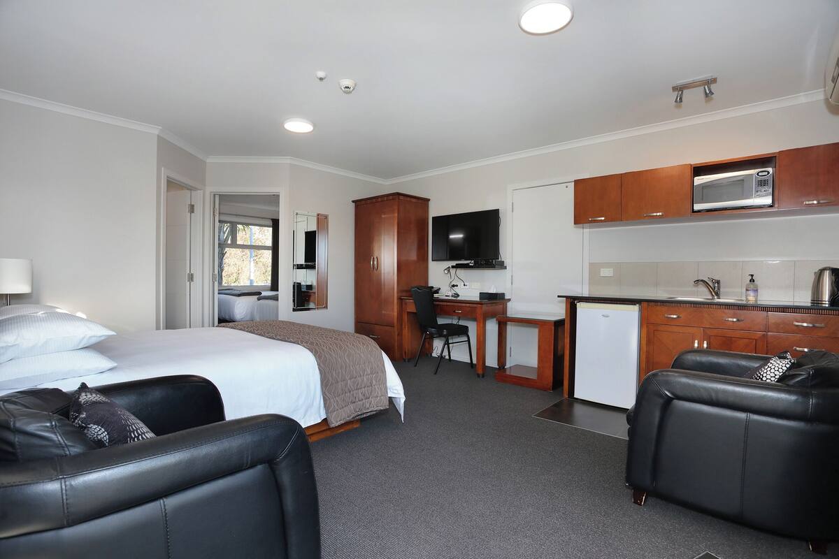 A hotel room with a bed, a desk, a kitchenette, and a seating area.