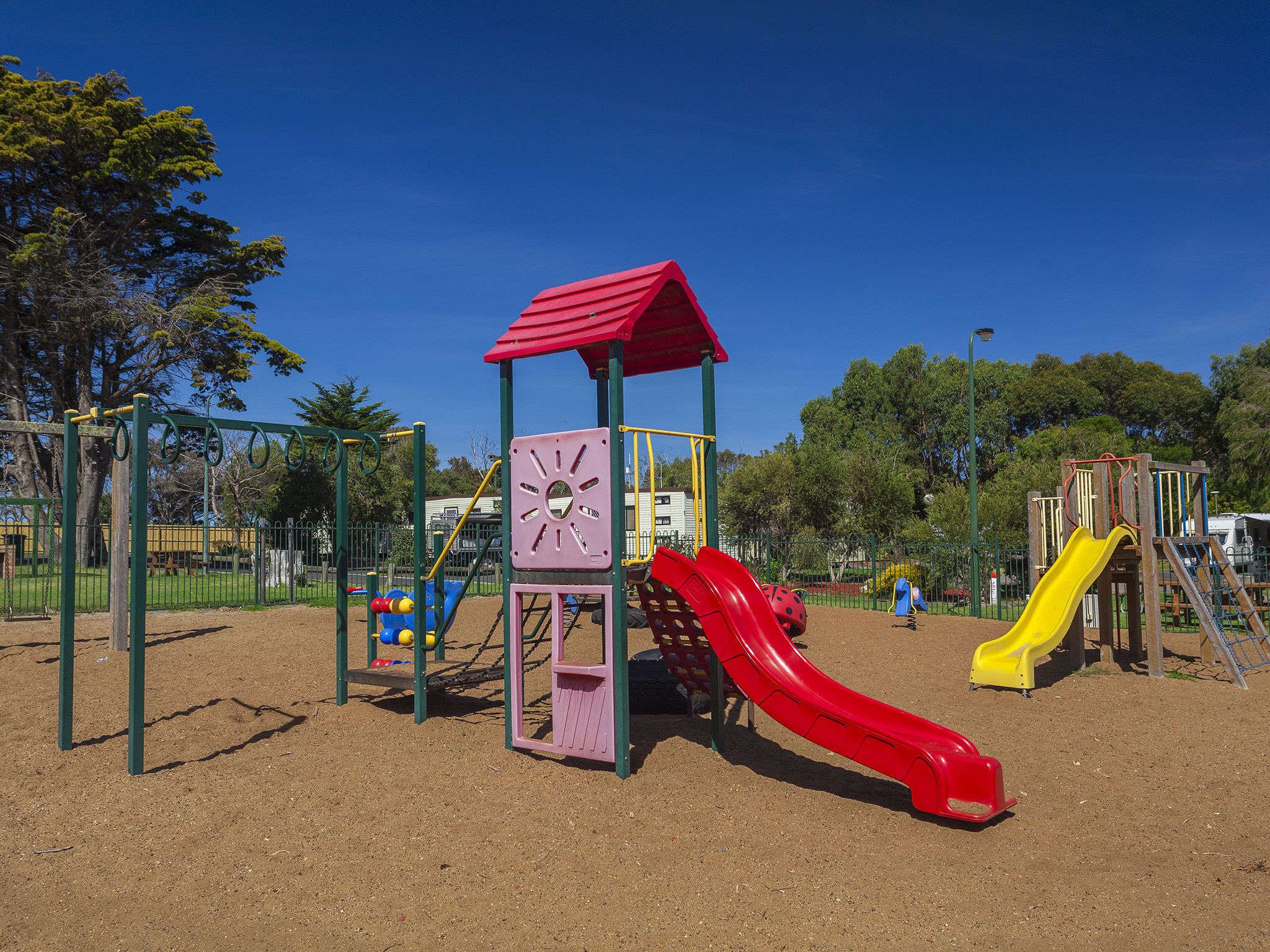 A playground with a red slide, a yellow slide, and a climbing structure.