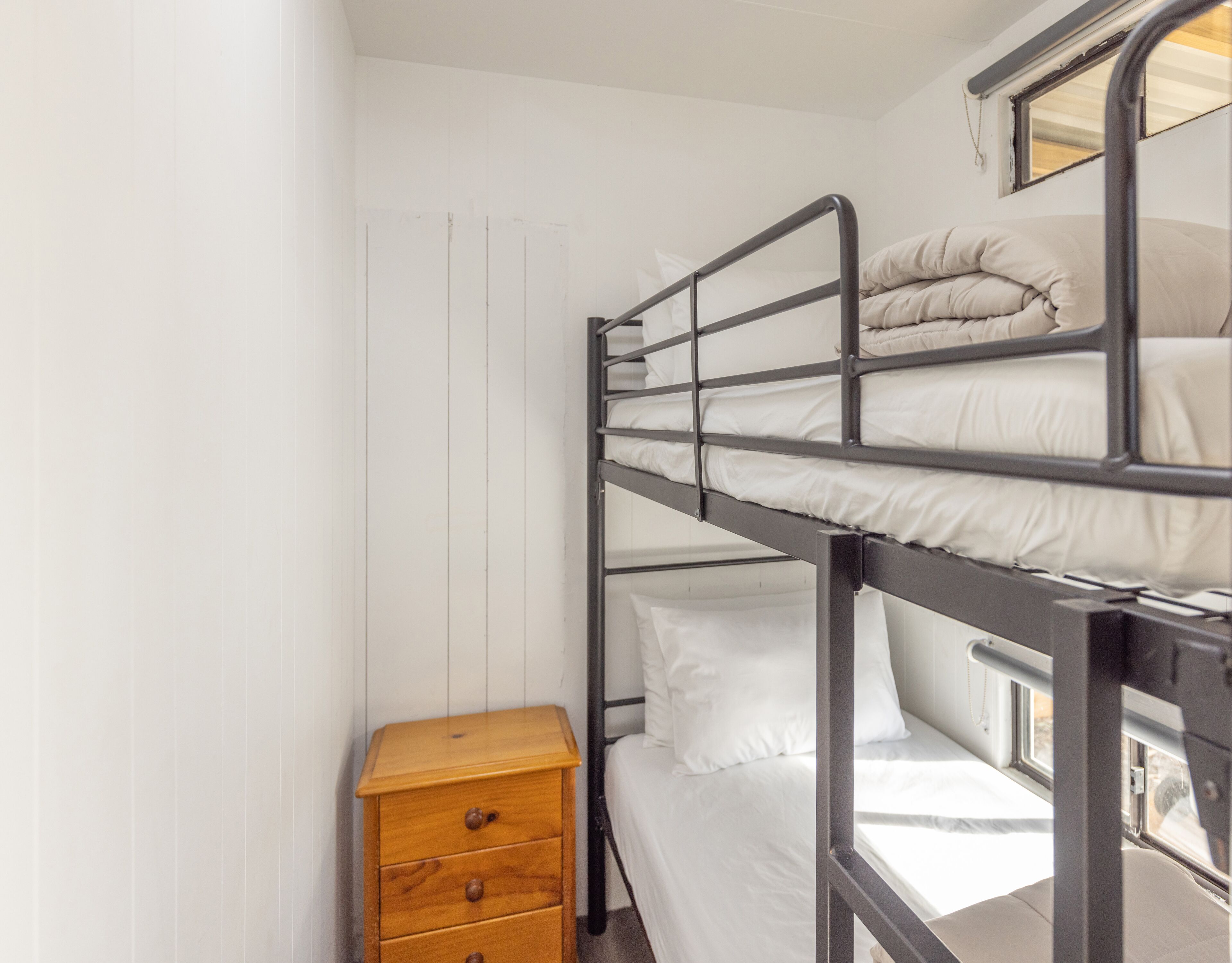 A bunk bed with white bedding and a wooden nightstand with drawers.