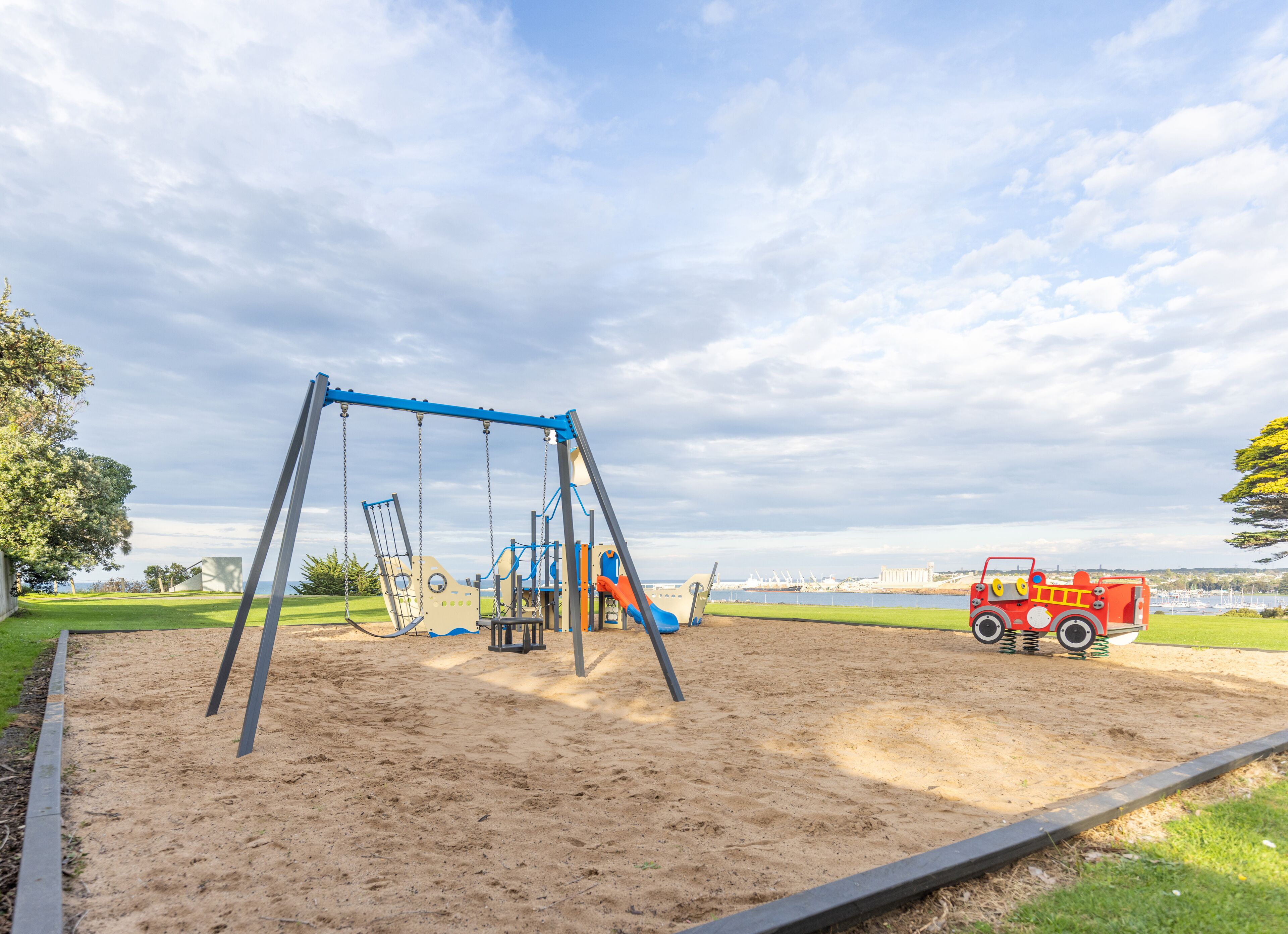 A playground with swings and slides, a sandbox, and a red toy fire truck.
