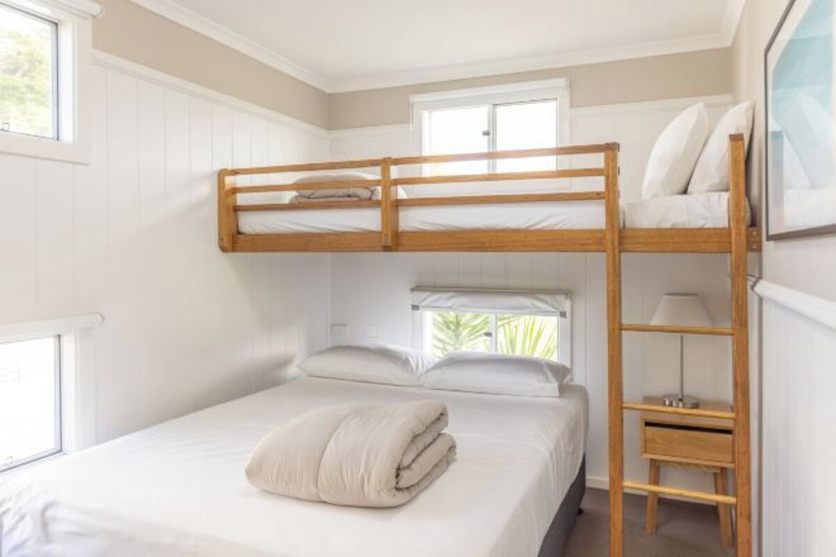 A bunk bed room with a window, a desk, and a lamp.
