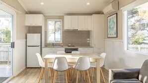 A modern kitchen with white cabinets, a wooden dining table, and chairs. - NRMA Portland Bay Holiday Park (Portland)