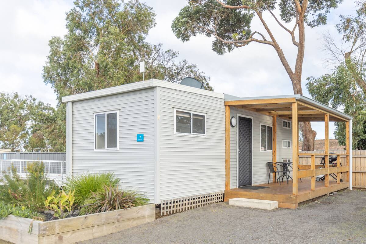 A small, single-story mobile home with a covered porch and a fenced garden area.