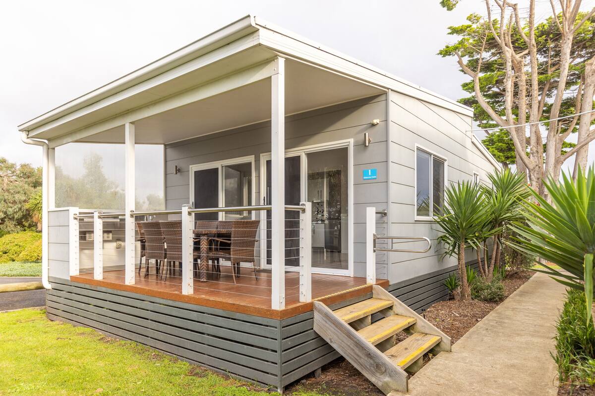A modern house with a covered porch, a dining area with outdoor furniture, and a small staircase leading to the entrance.