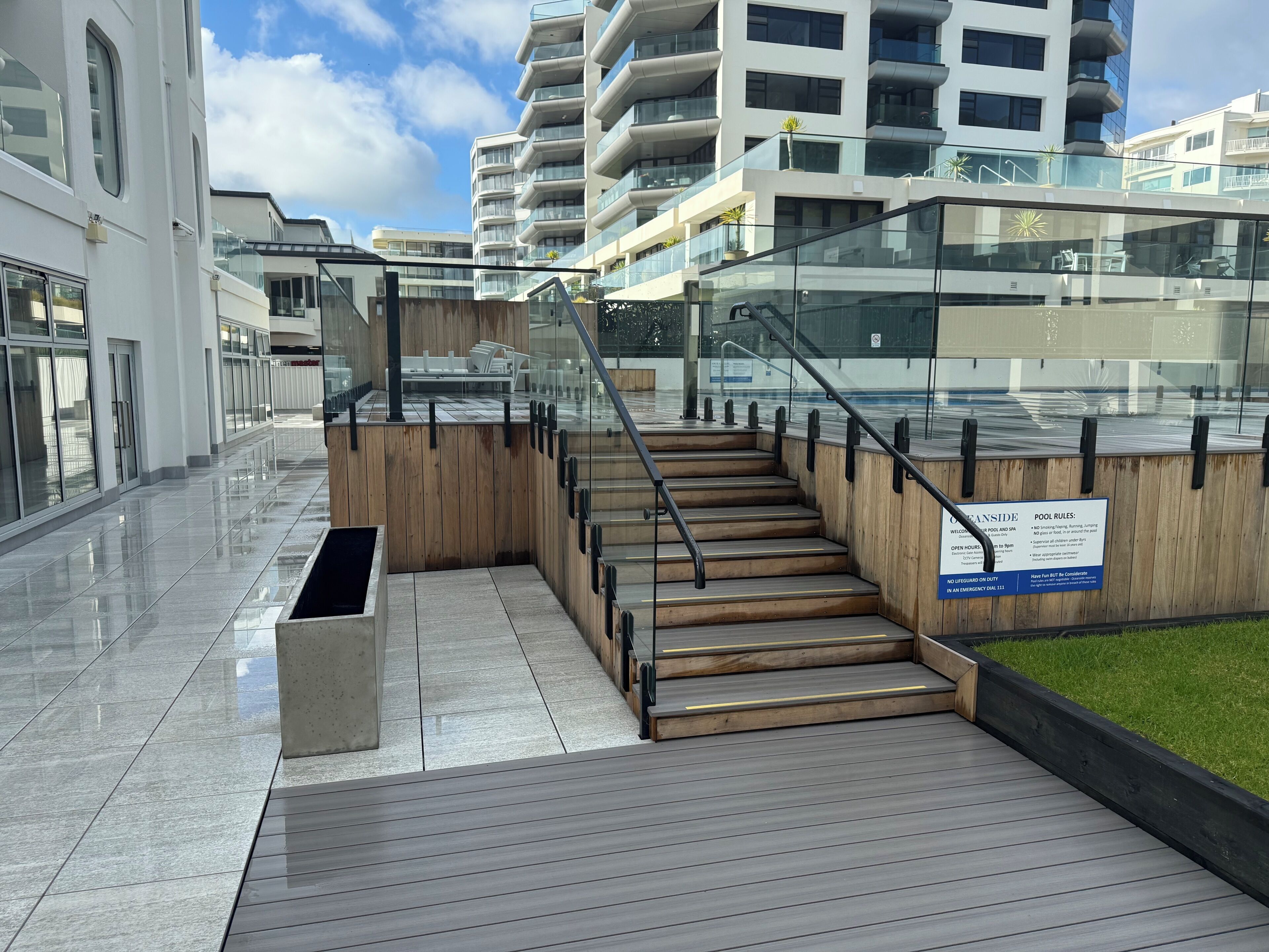 A modern building with a glass facade, a wooden staircase, and a sign indicating pool rules.