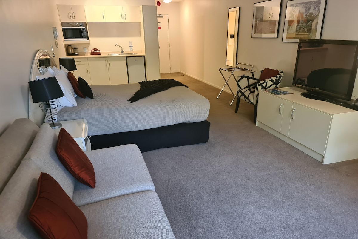 Ett modernt hotellrum med en soffa, en TV, ett litet bord och ett litet kök.