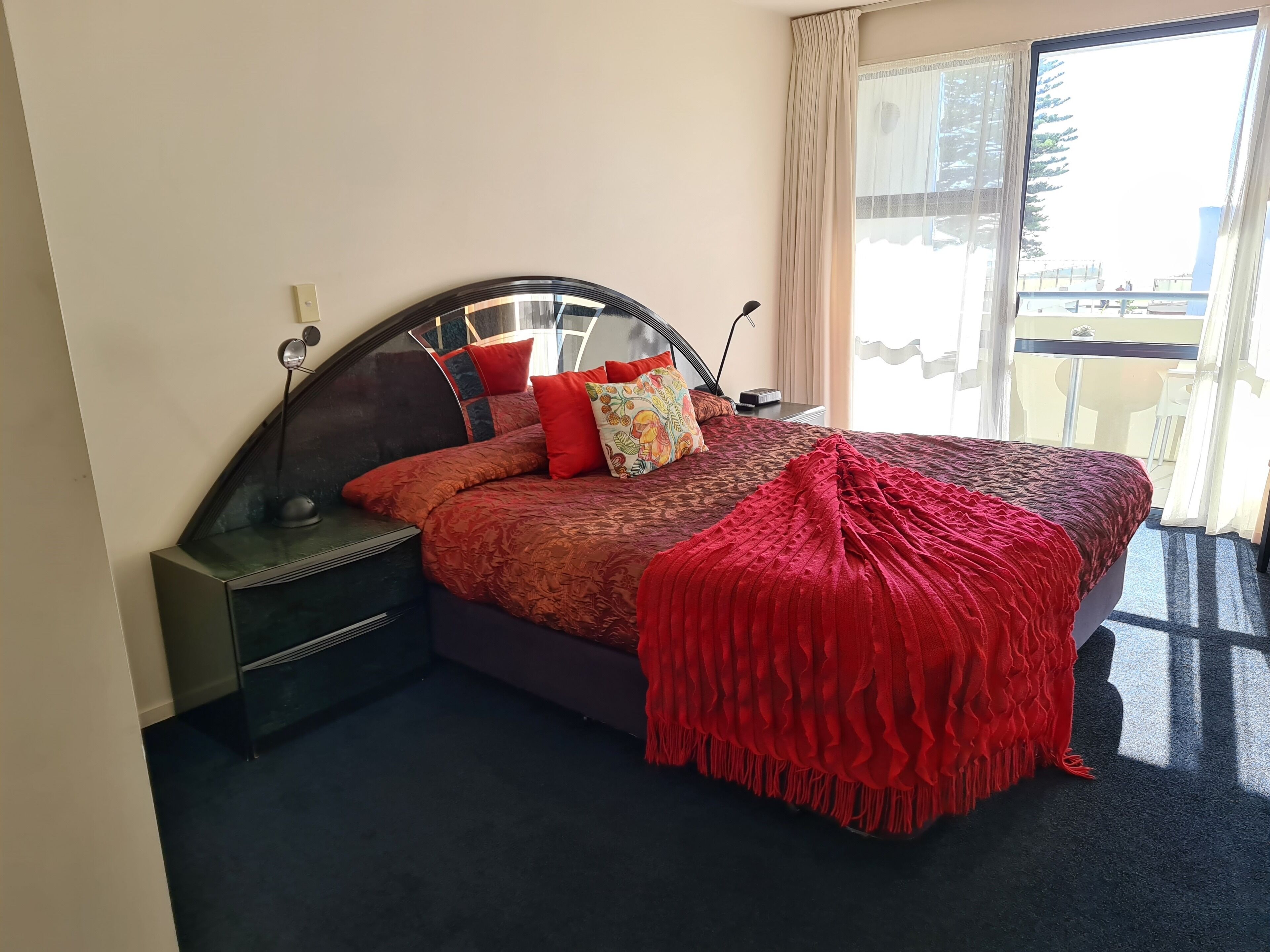 Een hotelkamer met een groot bed, een nachtkastje, een lamp en uitzicht op het balkon.