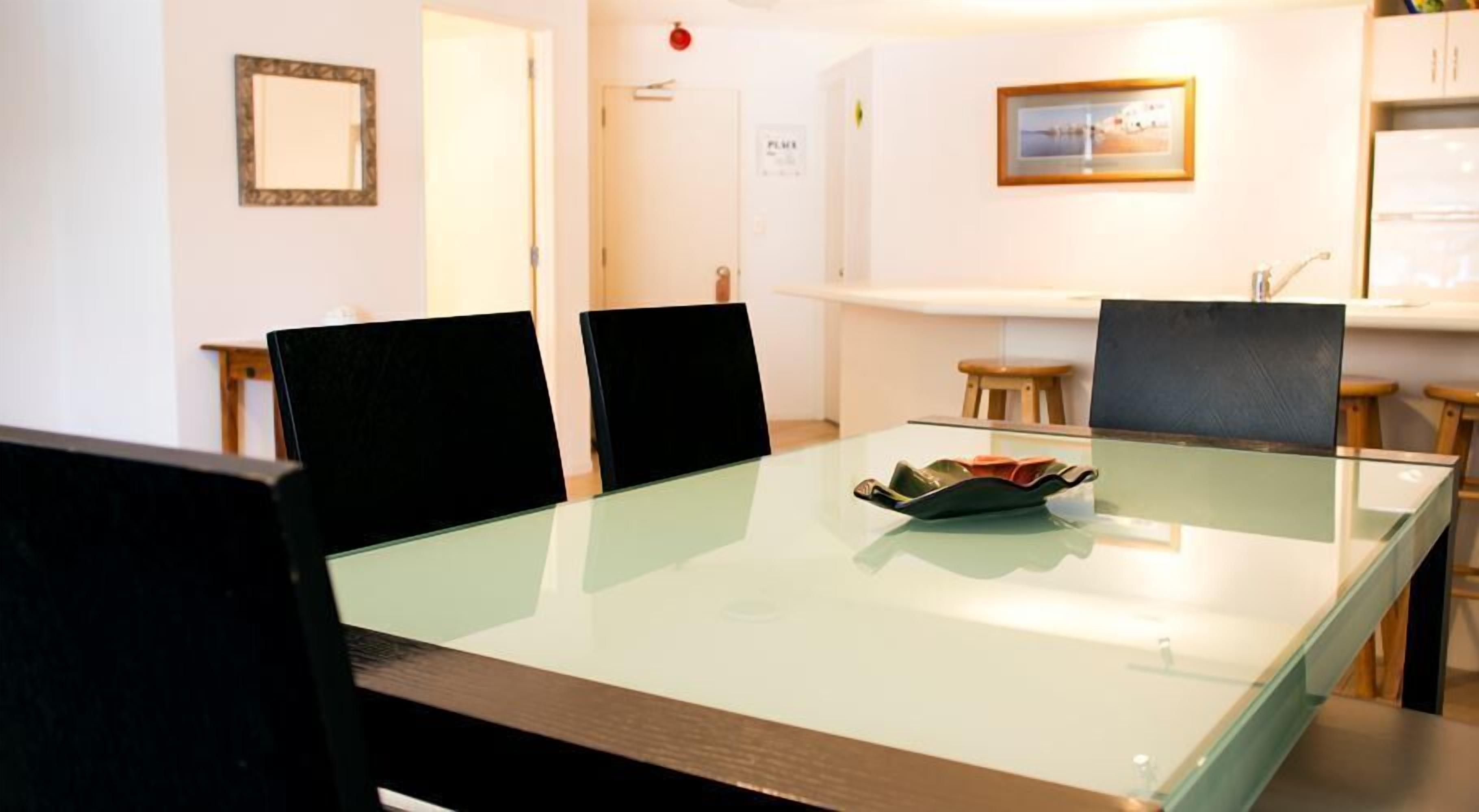 Un comedor con una mesa de vidrio, sillas negras y un pequeño cuenco decorativo.
