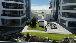 Un edificio moderno con varios balcones, un patio ajardinado con un tablero de ajedrez y vista a la playa.