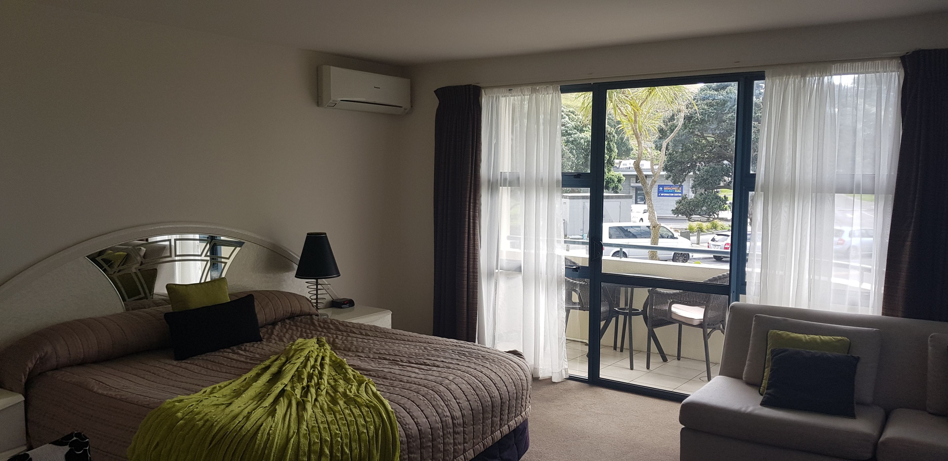 A hotel room with a bed, a chair, a table, and a view of the street through large windows.