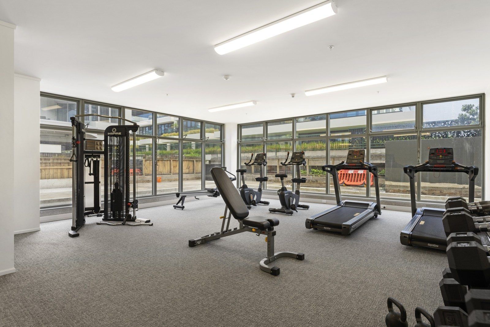 A gym with exercise equipment, large windows, and a view of the outside.