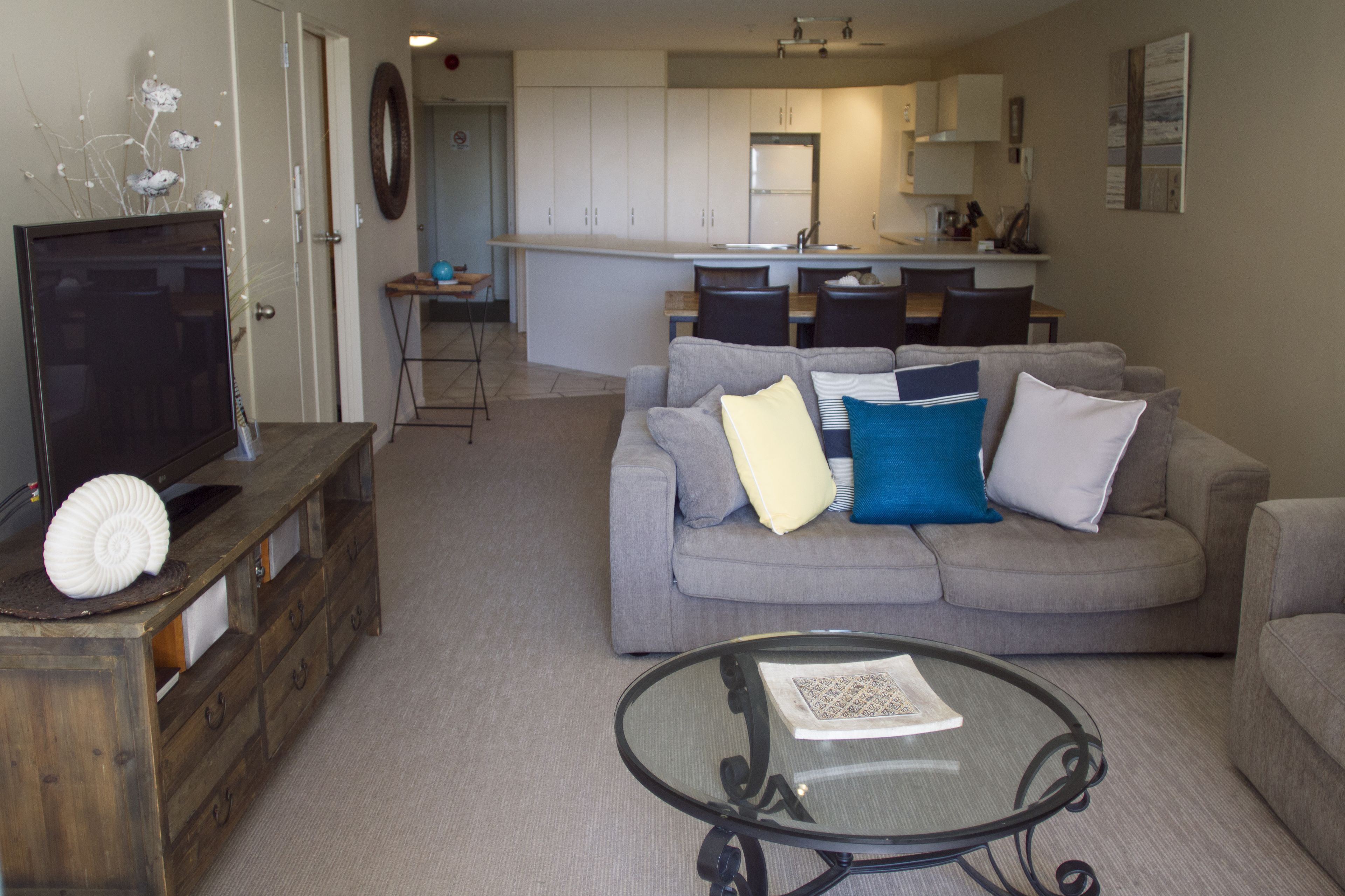 A living room with a grey sofa, a glass coffee table, and a wooden entertainment unit with a TV.