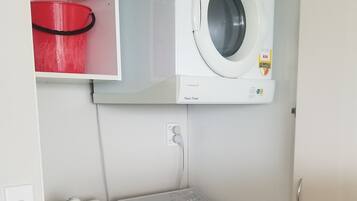Ett litet och praktiskt tvättrum med en tvättmaskin och en torktumlare som man matar från framsidan, ett handfat och en röd hink.