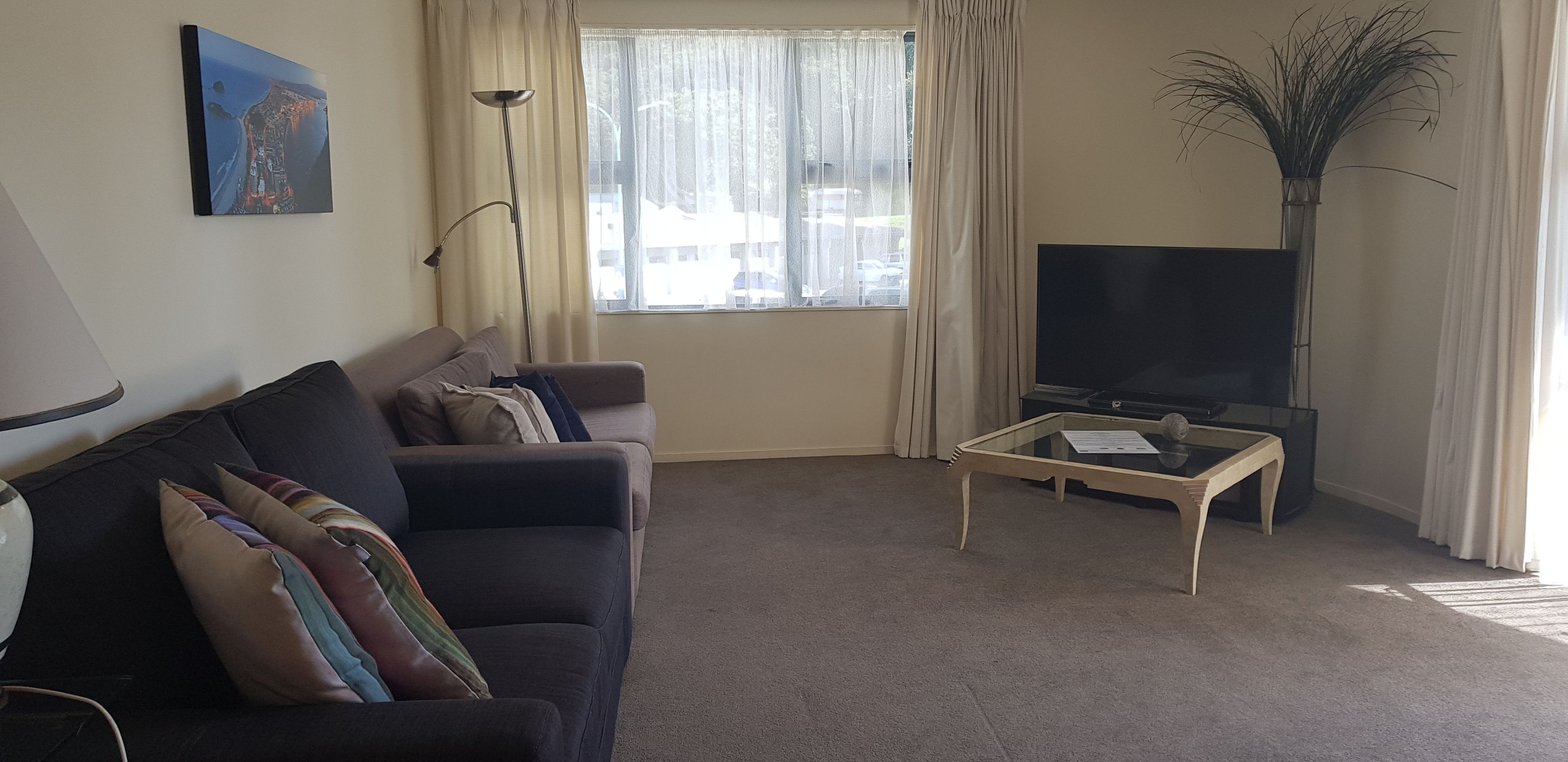 Una sala de estar con un sofá, una mesa de centro, un televisor y un ventanal con cortinas.