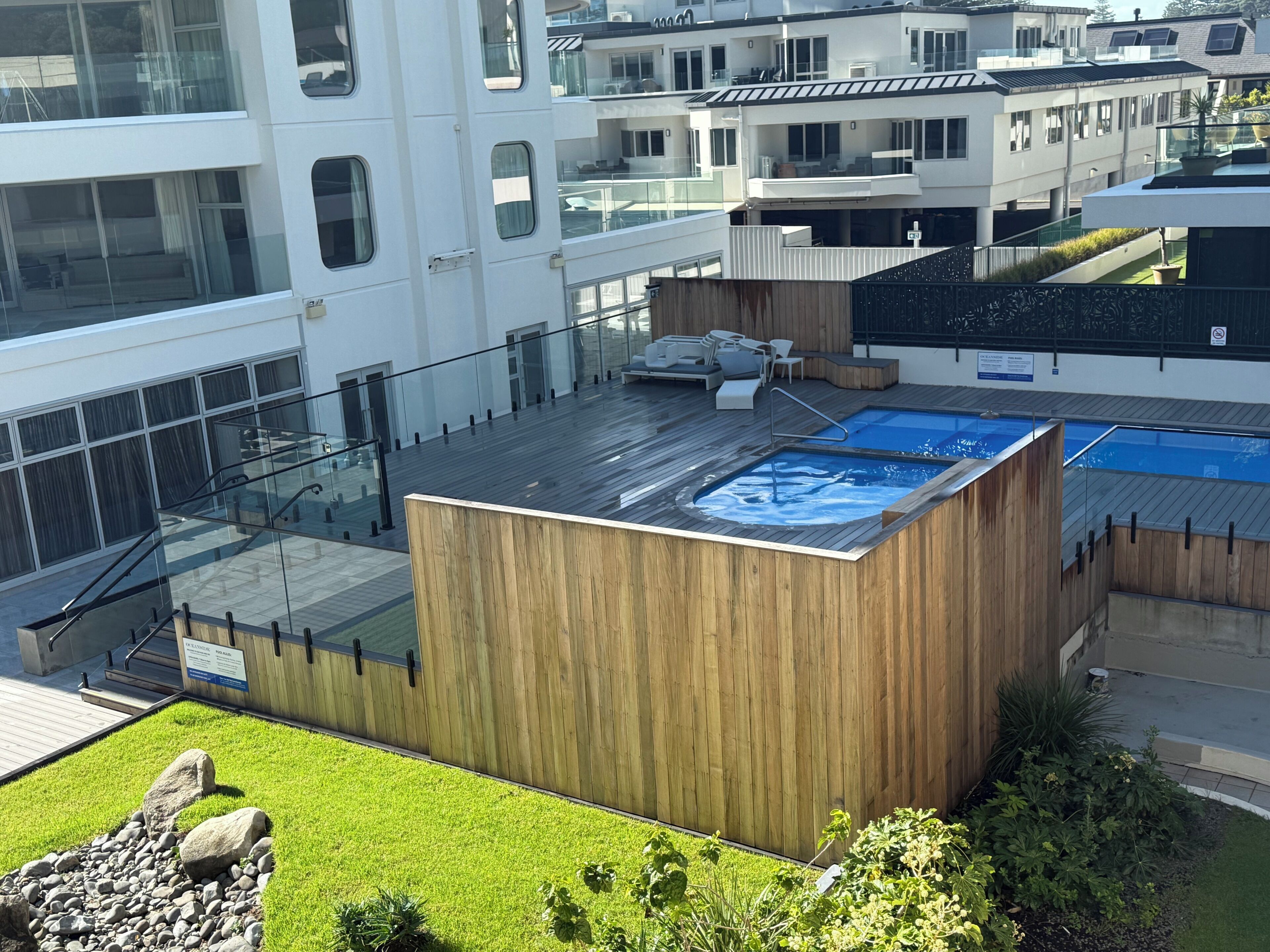 A modern building with a rooftop pool, glass railings, and a wooden deck.