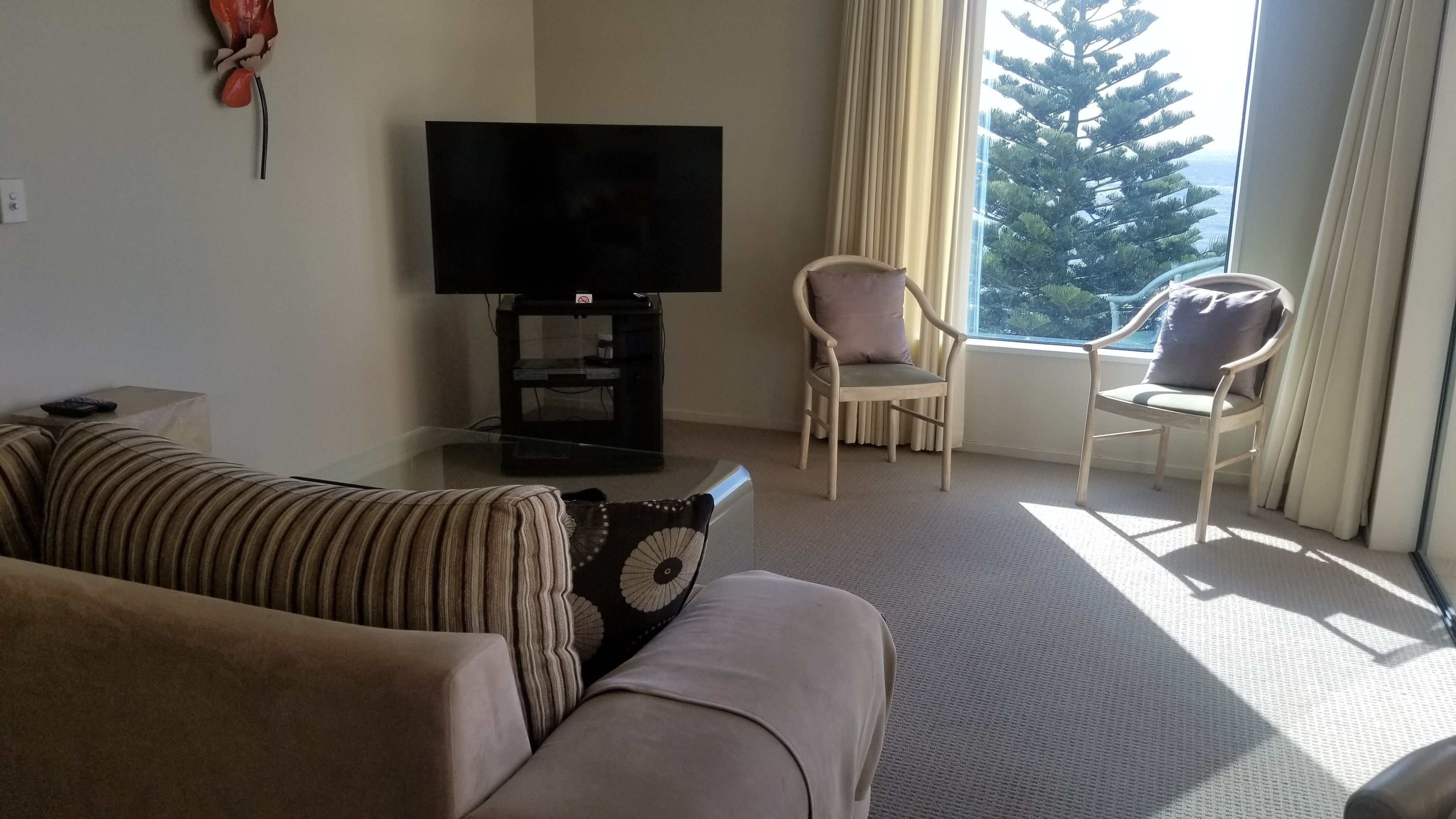 A living room with a sofa, a television on a stand, two chairs, and a window with curtains.