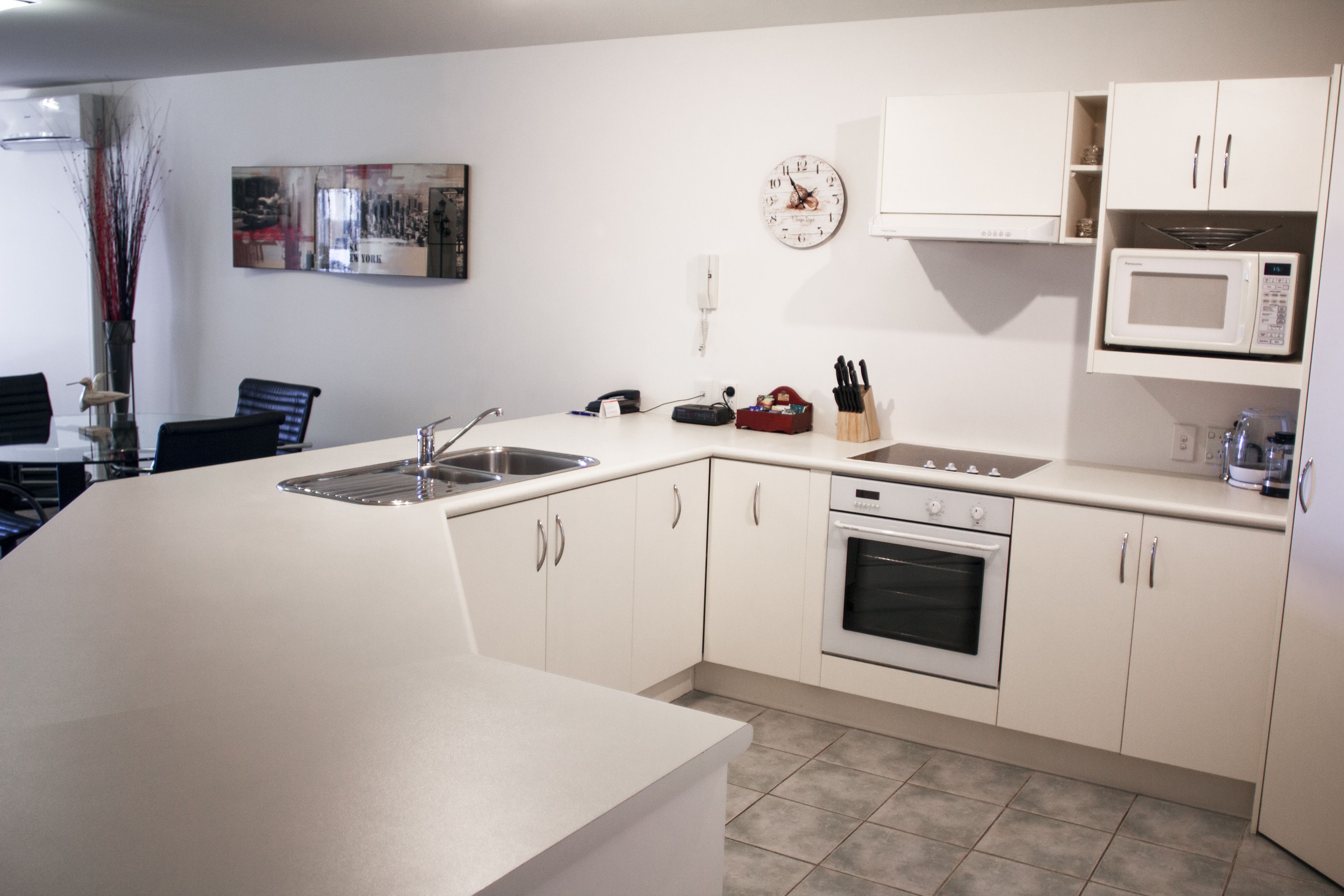 Una cocina moderna con armarios blancos, un lavamanos de acero inoxidable, un microondas y un horno.