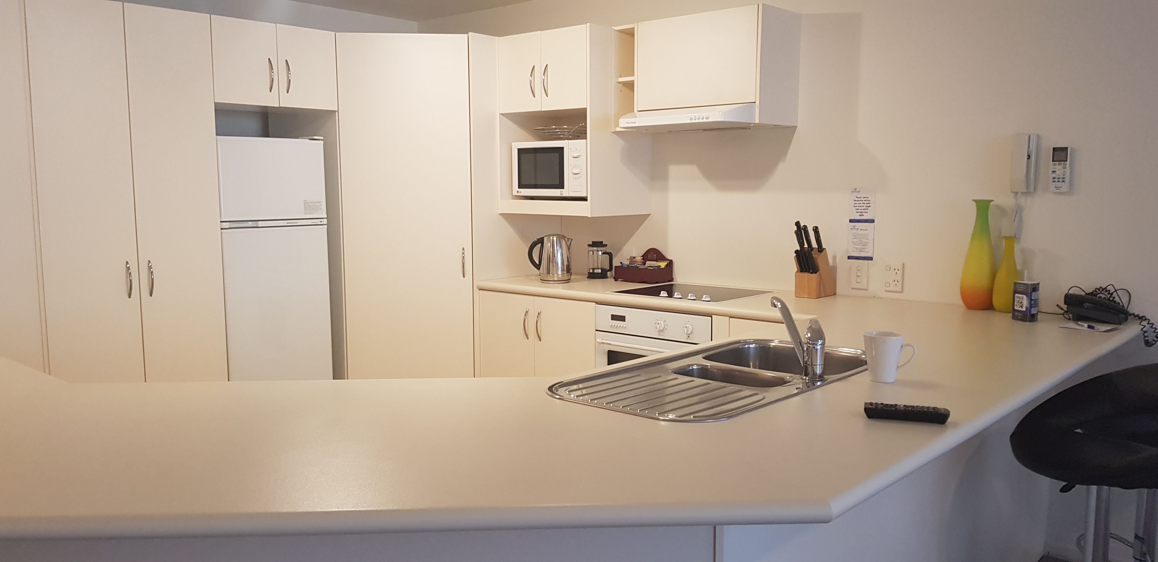 A modern kitchen with white cabinets, a microwave, a kettle, and a sink.
