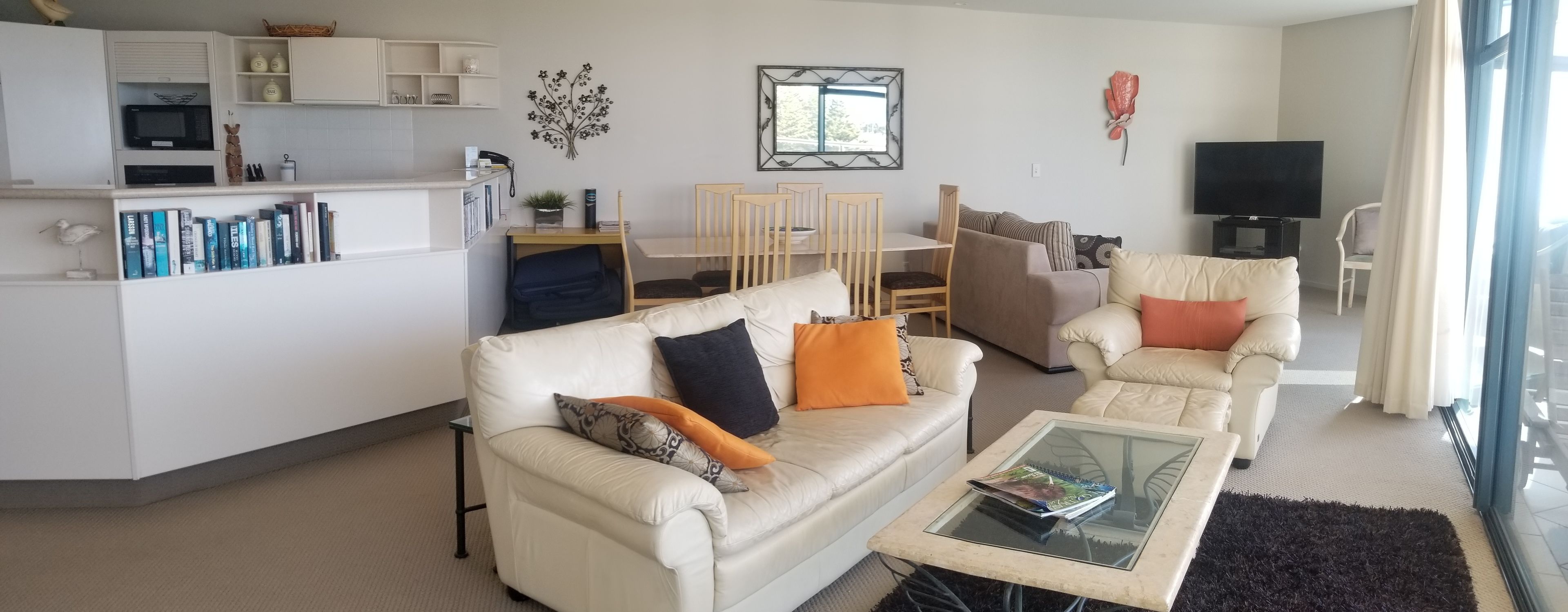 A modern living room with a sofa, armchairs, a coffee table, and a dining area with chairs and a table.