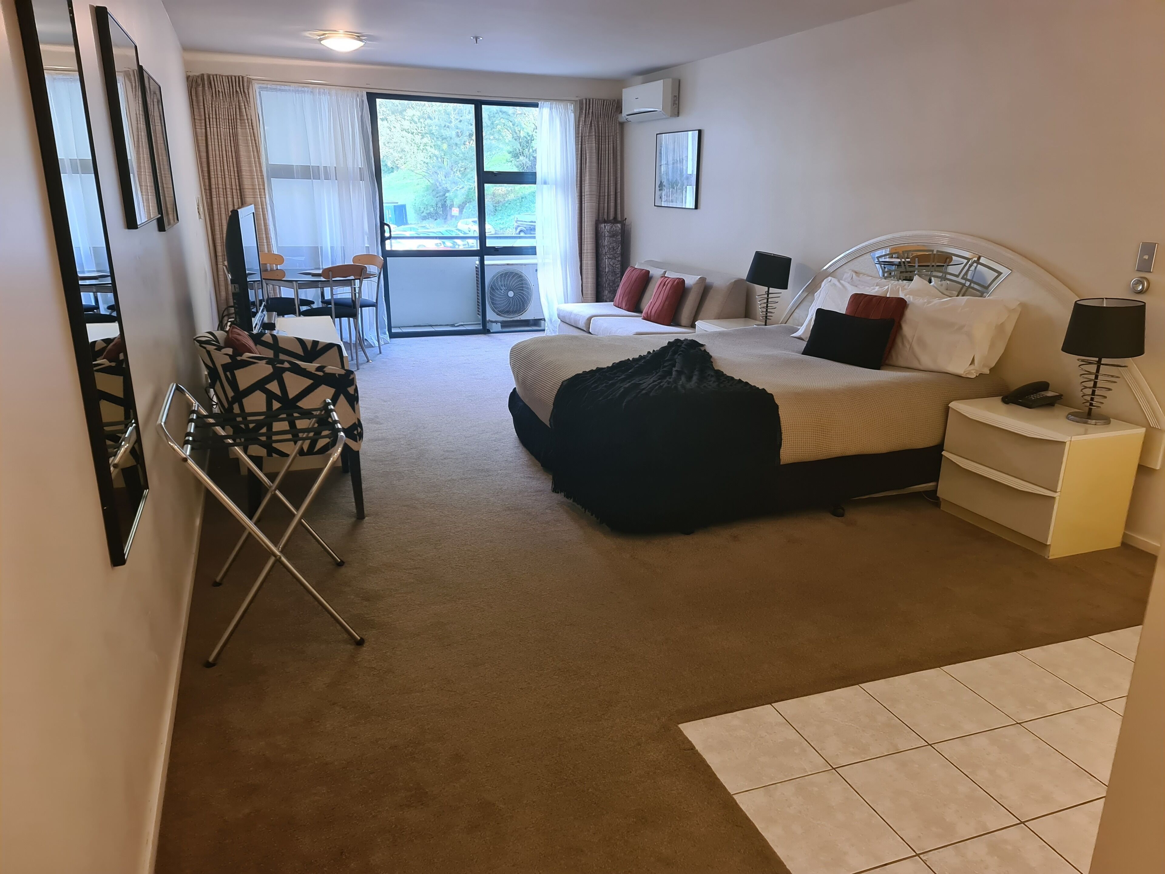 Une chambre d’hôtel avec un lit, une table de chevet, une lampe et une vue sur l’extérieur par une fenêtre.