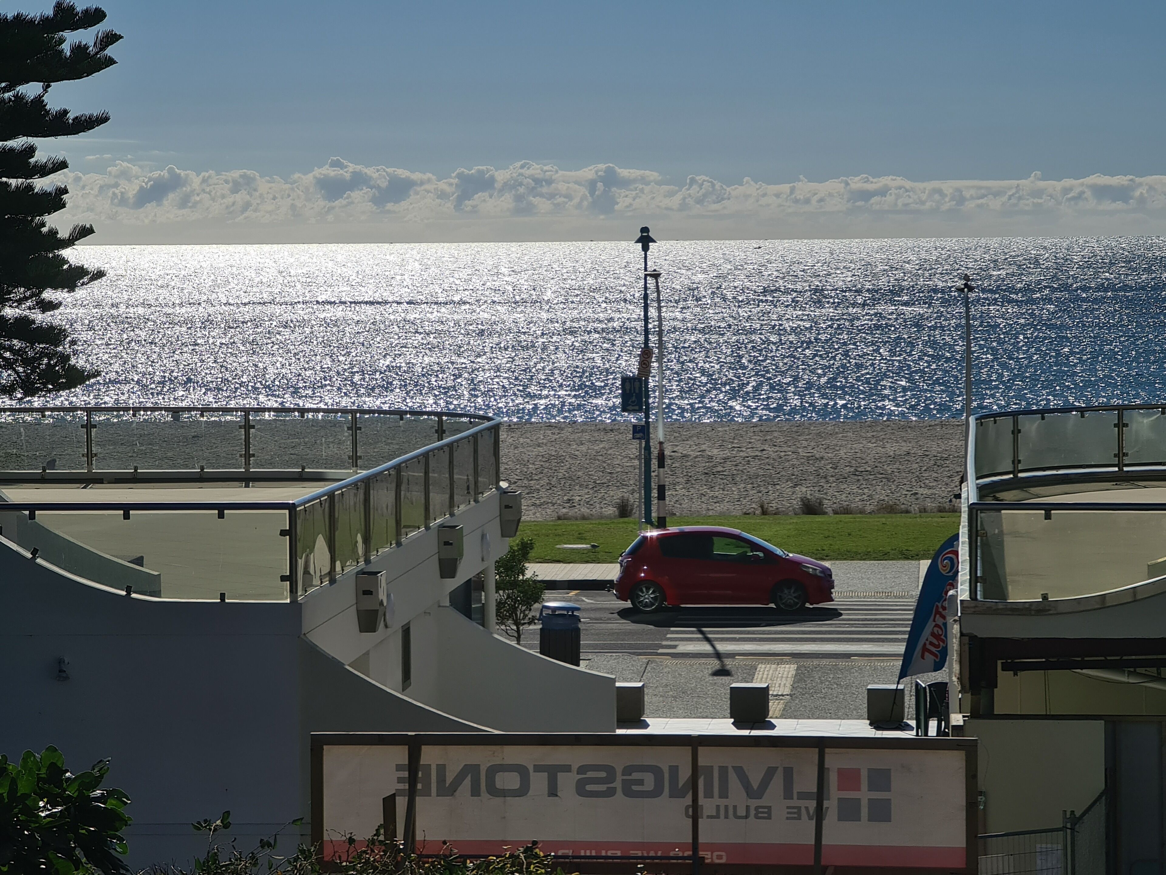 A view of a waterfront property with a red car parked in front, a building with a sign reading "LIVINGSTON," and a clear view of the sea and sky.