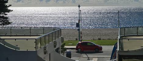 A view of a waterfront property with a red car parked in front, a building with a sign reading "LIVINGSTON," and a clear view of the sea and sky.