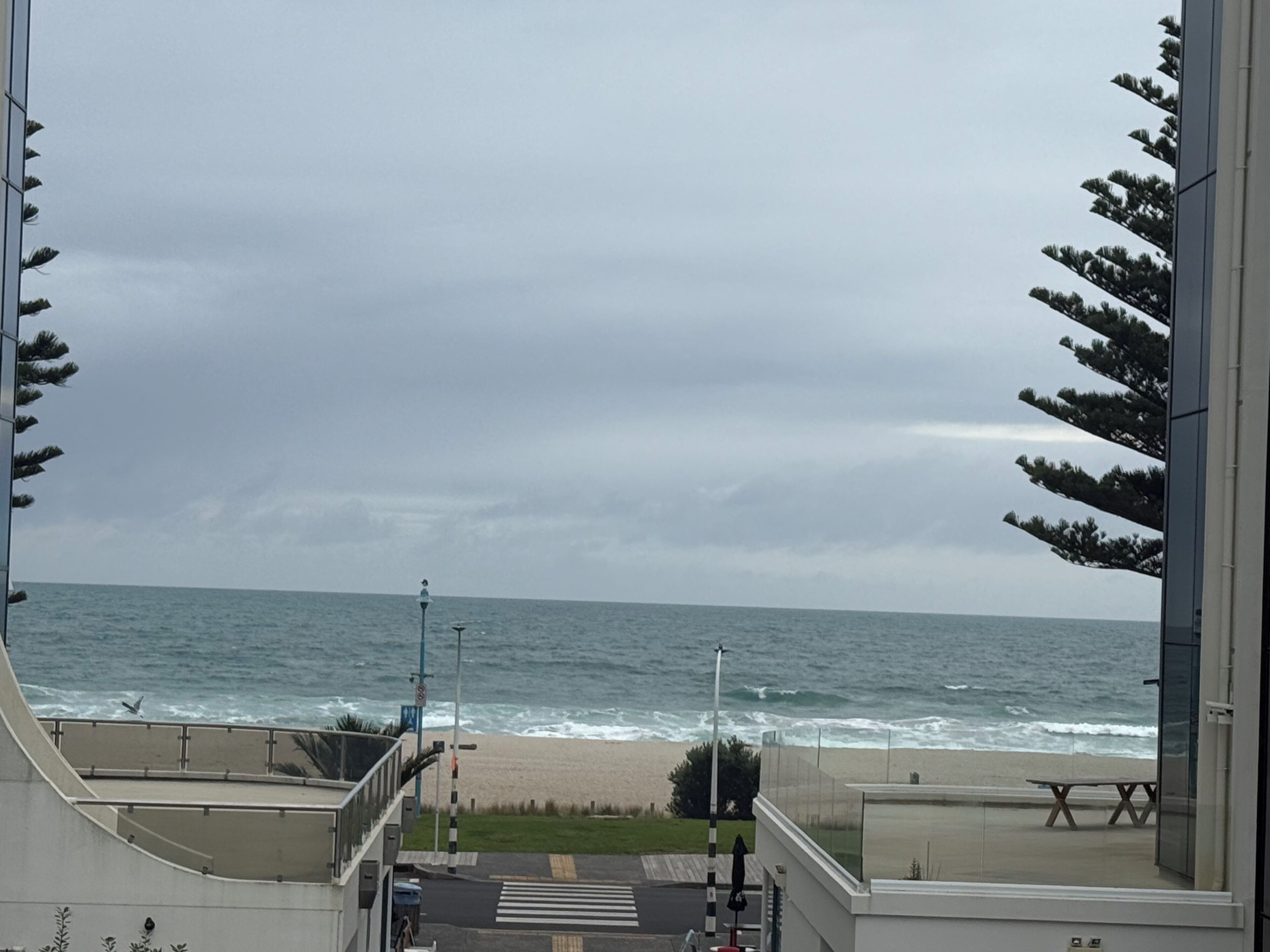 A view of the beach from a building with a glass balcony, a pedestrian crossing, and a street lamp.
