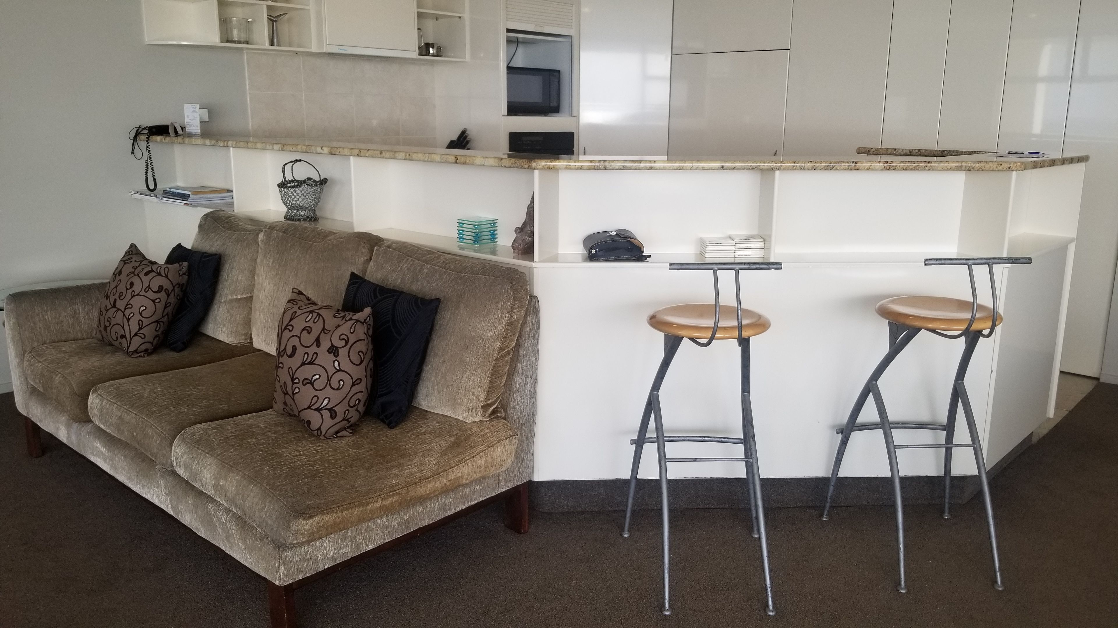 Un área de estar moderna con un sofá, dos taburetes de bar y una encimera de cocina.