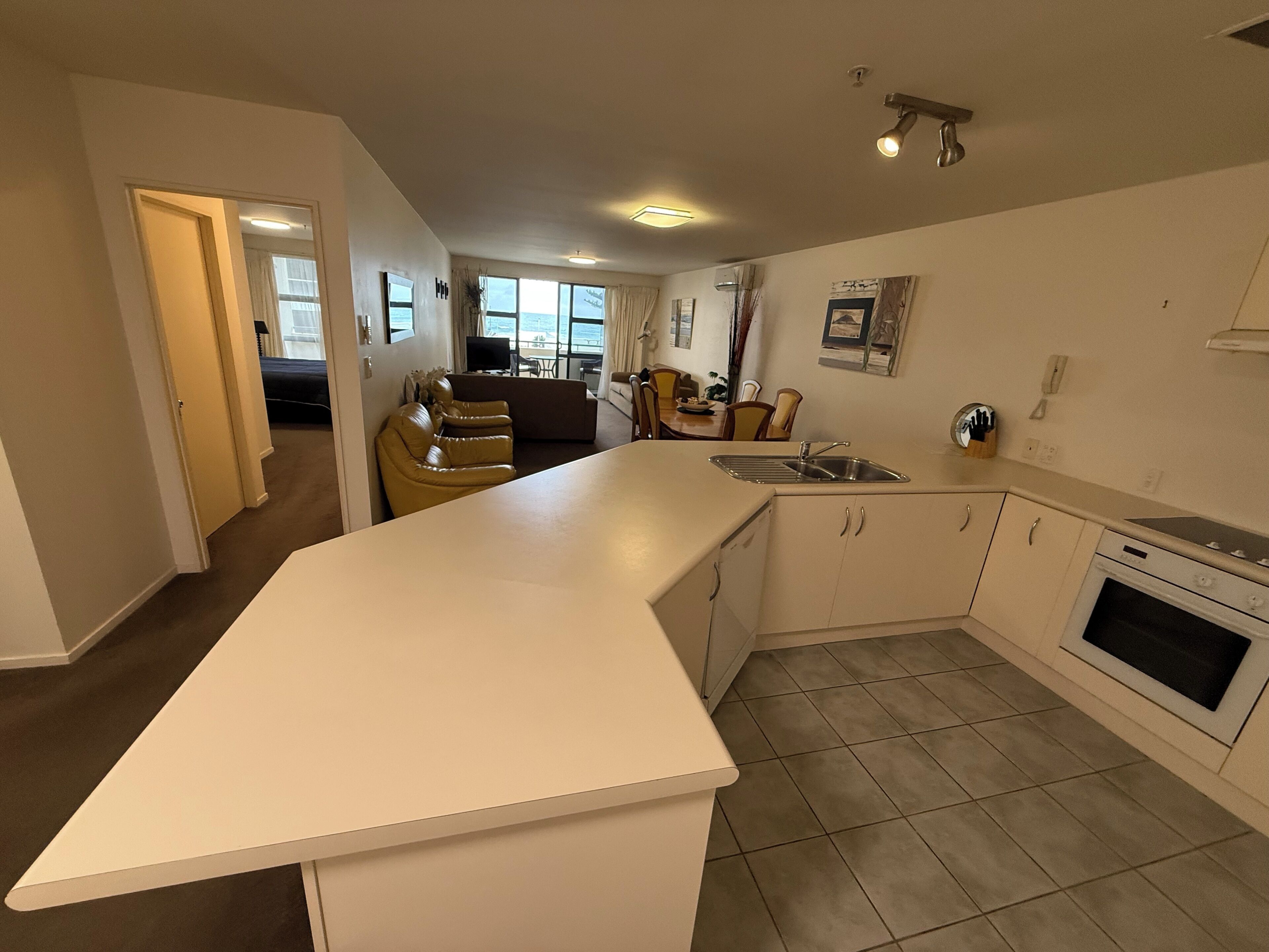 A modern kitchen with a large island, a dining area with a sofa and chairs, and a view through the windows.