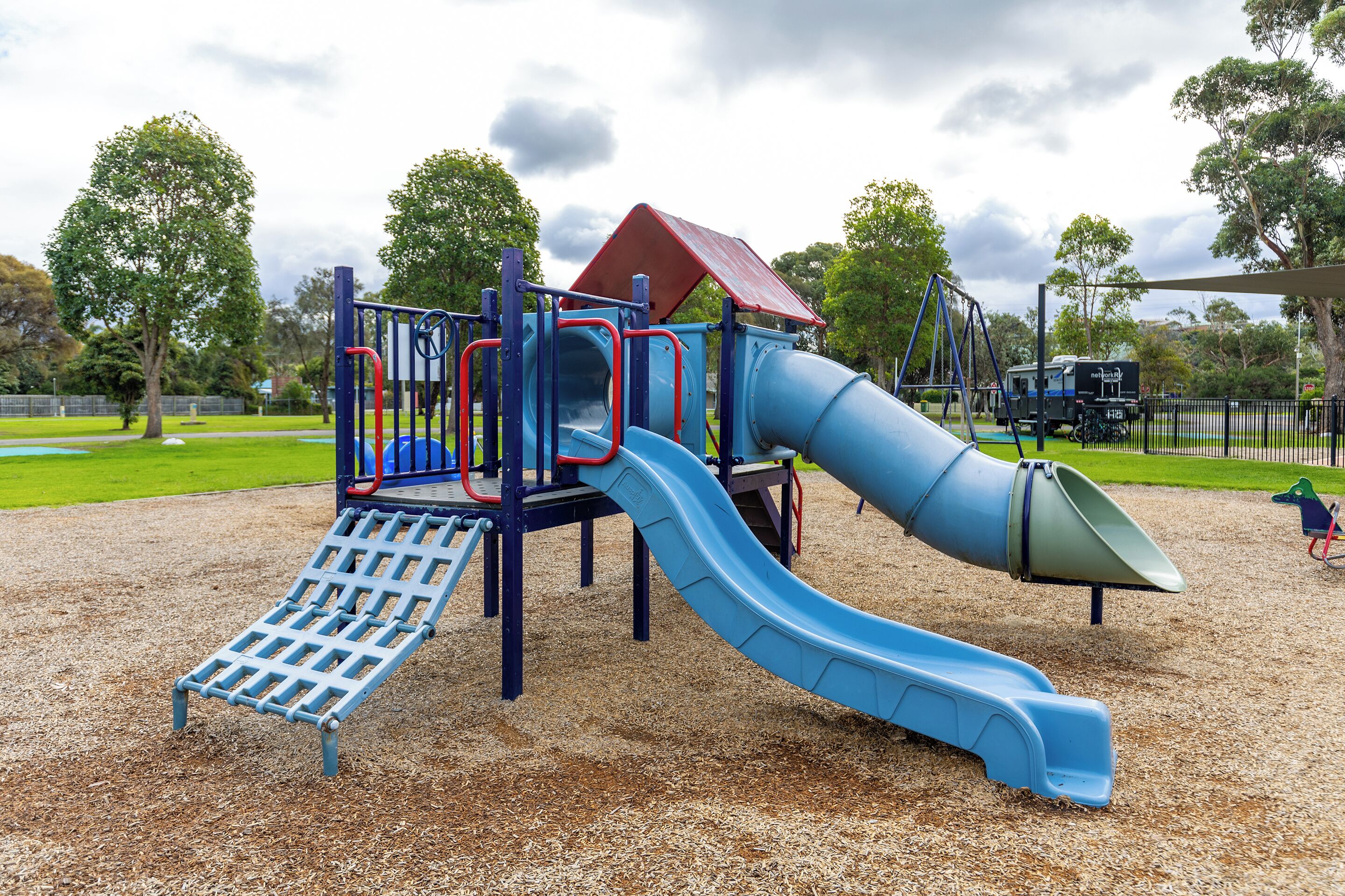 A playground with a blue slide, climbing structures, and a red-roofed playhouse.