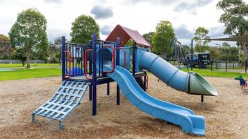 A playground with a blue slide, climbing structures, and a red-roofed playhouse.