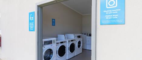 A laundry facility with multiple washing machines and dryers, a sign indicating washing machine and dryer costs, and a sign advising against washing pet bedding in machines.