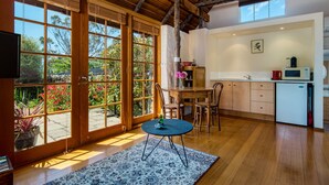 A spacious kitchen with wooden cabinets, a dining table, and a large window overlooking a garden. - Wagners Cottages (Swansea)