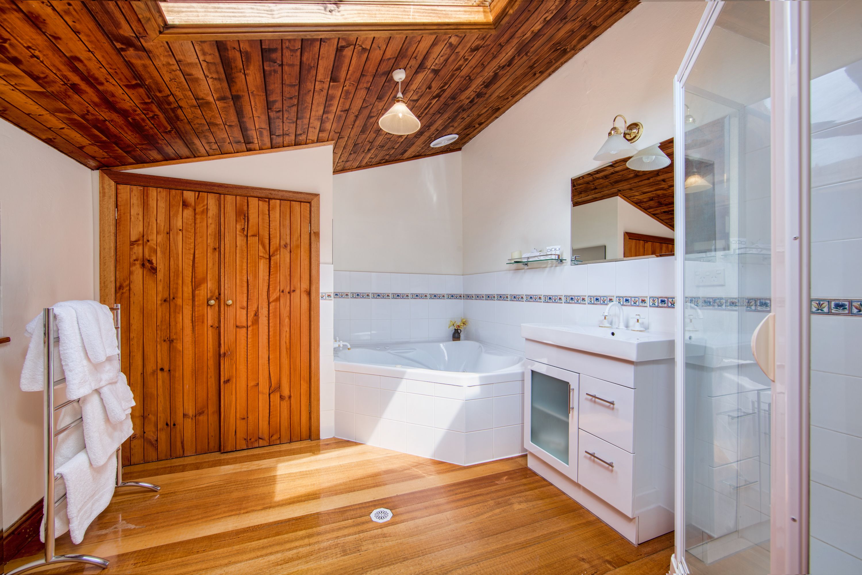 A bathroom with a wooden ceiling, a bathtub, a glass shower enclosure, and a white sink.