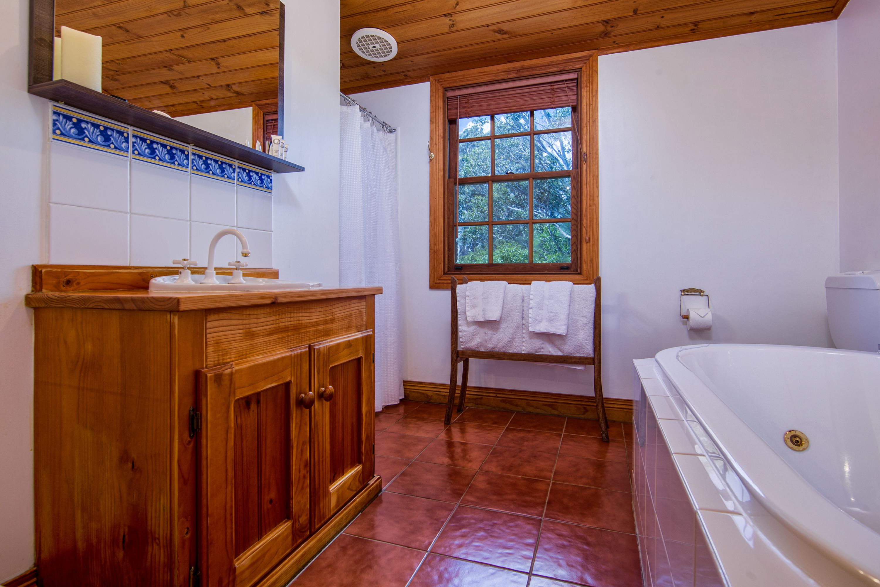 A bathroom with a wooden vanity, a bathtub, a window with a view of trees, and a tiled floor.