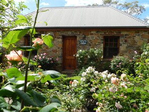 A stone building with a wooden door and windows, surrounded by a garden with various flowers.